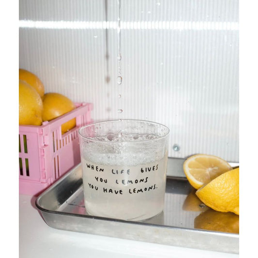 Verre transparent avec citation manuscrite “When life gives you lemons you have lemons” sur fond blanc