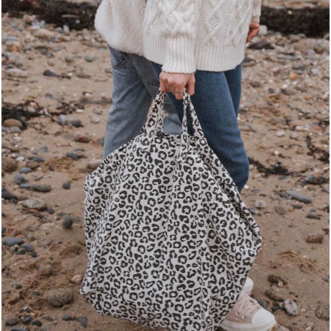 sac cabas Graou Grège Rose in April porté sur la plage, imprimé léopard noir sur fond écru