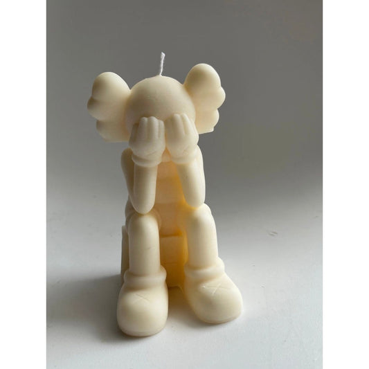 Bougie ivoire représentant un personnage assis la tête dans les mains, inspirée de Kaws