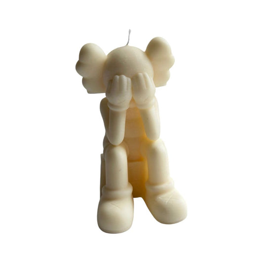 Bougie ivoire représentant un personnage assis la tête dans les mains, inspirée de Kaws