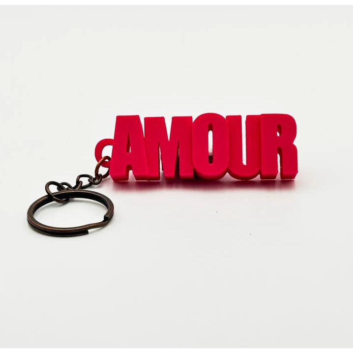 Porte-clés rose AMOUR en lettres majuscules, présenté dans un tube à essai avec bouchon en liège, sur fond rose – Mauvaises Graines