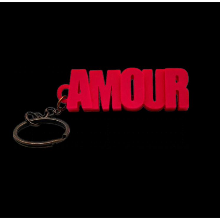 Porte-clés rose AMOUR en lettres majuscules, présenté dans un tube à essai avec bouchon en liège, sur fond rose – Mauvaises Graines