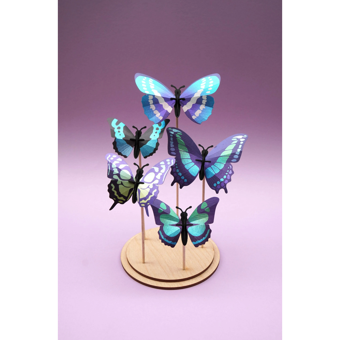 Ensemble de quatre papillons 3D Assembli en papier bleu, turquoise et violet présenté dans un cadre en bois